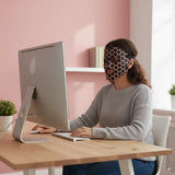 Person wearing a honeycomb-patterned mask sitting at a desk with a computer.