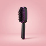 A black and purple paddle hairbrush standing upright on a pink studio background.