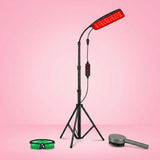 A red LED light therapy panel on a black tripod stand, shown with a green face mask and a gray hair brush against a pink gradient background.